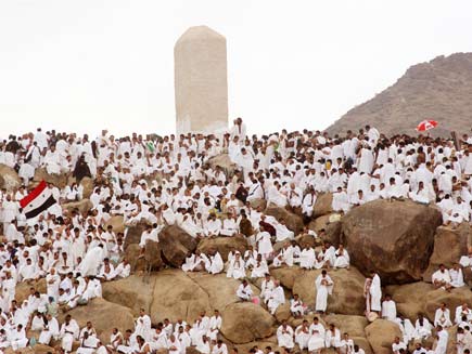 Mountain on the plain of Arafat where dozens of people dressed in white sit in contemplation and prayer