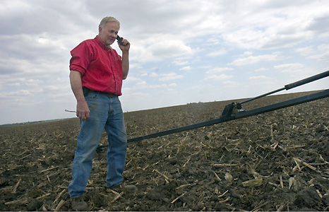 Man on phone next to farming equipment. Photograph by Elena Rue, Center for Documentary Studies at Duke University.