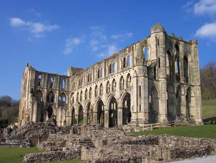 The ruins of the church at Rievaulx Abbey: a shell of a building, stone walls and window arches largely intact but no roof