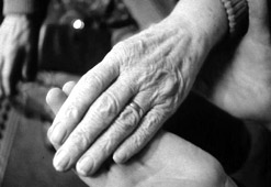 A carer holds an elderly woman's hand