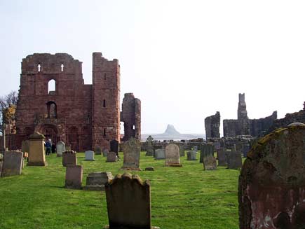 The ruins of Lindisfarne Priory: only a few broken sections of stone wall remain standing. Old, irregularly spaced gravestones can be seen in the foreground