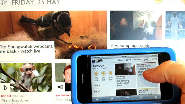 Mobile phone with blue case viewing the mobile homepage, in front of the bbc.co.uk homepage