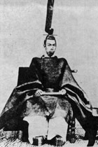 Emperor Meiji sitting in his full court robes. Extremely wide sleeves and wide trousers are visible and he is wearing a very tall and narrow hat