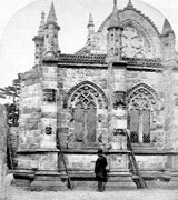 Black-and-white photograph of a man standing under the wall of Rosslyn Chapel