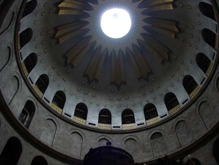 Inside of the Church of the Holy Sepulchre dome. Light streams in from the opening at the top, illuminating the gold sunburst and star patterns on the ceiling
