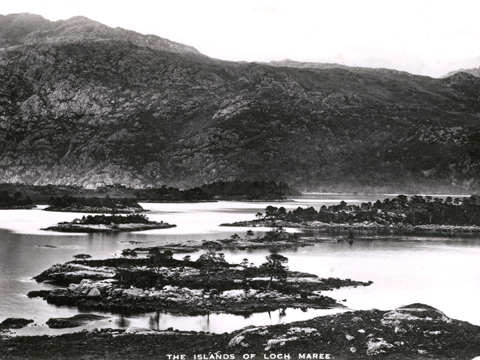 Black and white view looking across the islands of Loch Maree to mountains beyond.
