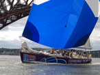 Edinburgh Inspiring Capital and crew passing under the Forth Rail Bridge, flying saltire spinnaker